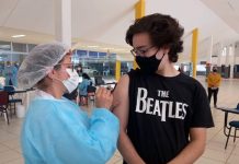 Vacinação contra Covid em adolescentes - rapaz usando camiseta dos beatles olha para enfermeira aplicando dose em seu braço