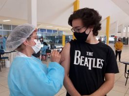 Vacinação contra Covid: Palhoça vacina a partir de 12 anos e São José 14 anos Vacinação contra Covid em adolescentes - rapaz usando camiseta dos beatles olha para enfermeira aplicando dose em seu braço