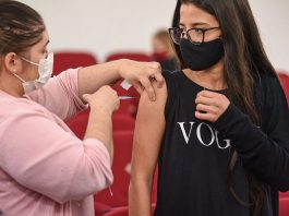 garota recebe vacina no braço olhando para enfermeira