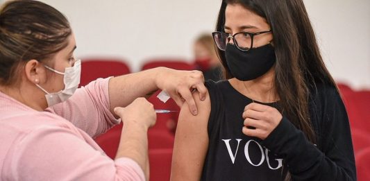 garota recebe vacina no braço olhando para enfermeira