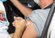 A foto foca na mão de uma pessoa aplicando a vacina em um braço de outra pessoa, sentada em um carro. A imagem ilustra a notícia de que São José vai atualizar os pontos de aplicação da 2ª dose da vacina contra a covid-19
