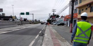 Acesso da BR-101 ao Kobrasol é interditado por duas semanas - trabalhador da concessionária com colete e capacete de EPI visto de costas na calçada ao lado da marginal da BR-101 em São José