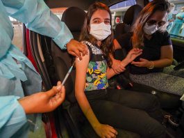 Mais de 60% da população catarinense vacinável está imunizada contra Covid garota bem jovem é vacina contra covid no braço dentro de carro; ela está de máscara e há uma mulher no banco do motorista