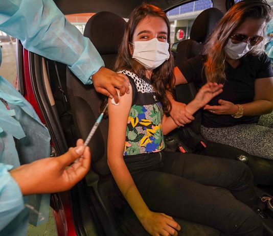 91% da população vacinável em SC recebeu ao menos uma dose contra Covid garota bem jovem é vacina contra covid no braço dentro de carro; ela está de máscara e há uma mulher no banco do motorista