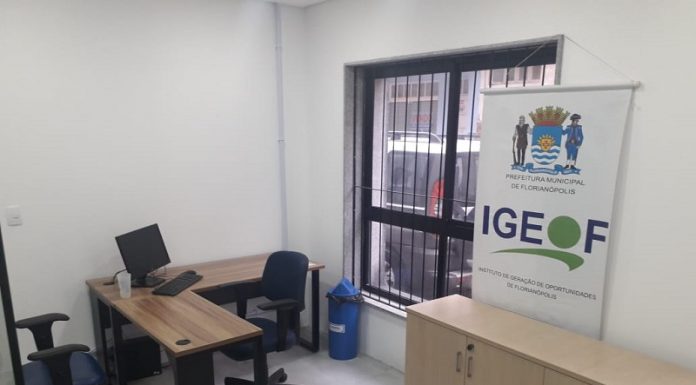 sala da nova sede do sine de florianópolis com mesa com computador alguns móveis e banner do igeof ao lado de janela