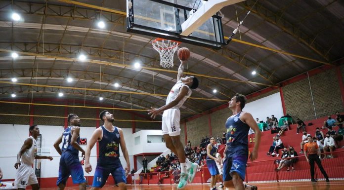 jogador se estiva com a bola na mão direita em direção à sexta observado por demais jogadores e público na arquibancada - O ginásio Nedir Valdo Macedo, em Barreiros, São José, recebeu seu primeiro jogo oficial