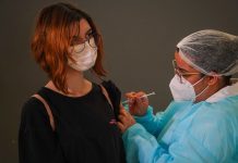 garota usando máscara e óculos recebe injeção no braço dada por enfermeira usando epi - Vacinação em SC: municípios têm disponíveis vacinas suficientes para a primeira dose em 100% dos adolescentes