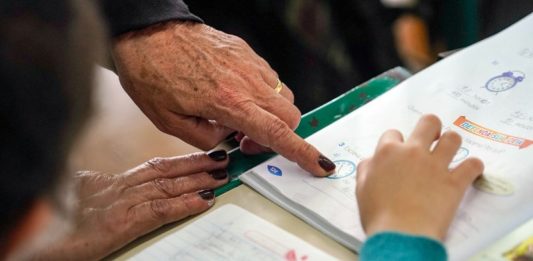 close em mão de professora apontando algo em livro para aluna - magistério estadual professores do estado reajuste salarial profisssionais de educação