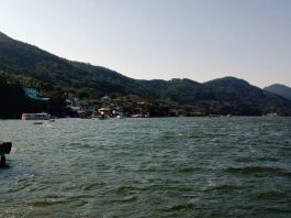 costa da lagoa vista da altura da água com montanhas e algumas casas em meio à vegetação