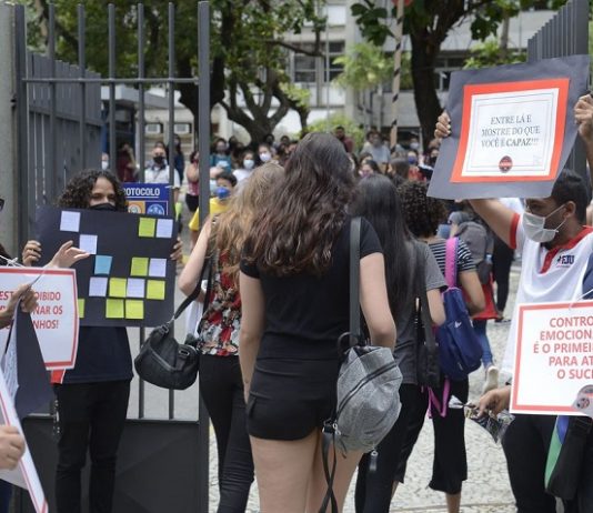 estudantes entrando em local de provam com pessoas no portão segurando cartazes e de máscara - Segundo dia do Enem tem provas de matemática e ciência da natureza