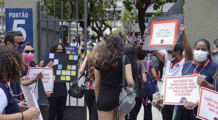 estudantes entrando em local de provam com pessoas no portão segurando cartazes e de máscara - Segundo dia do Enem tem provas de matemática e ciência da natureza