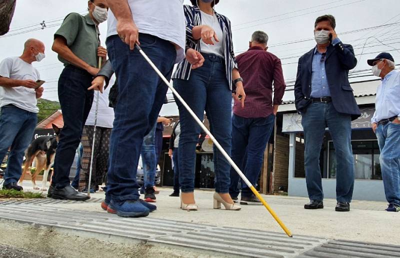 cego passa pelo piso tátil tocando com a vara observador por outras pessoas na calçada