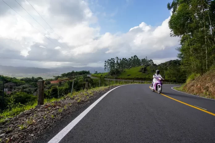 previsão do tempo | clima para amanhã em santa catarina: sol com algumas nuvens | mulher passando de biz em estrada do interior com grande pedaço de céu com nuvens e vale ao fundo