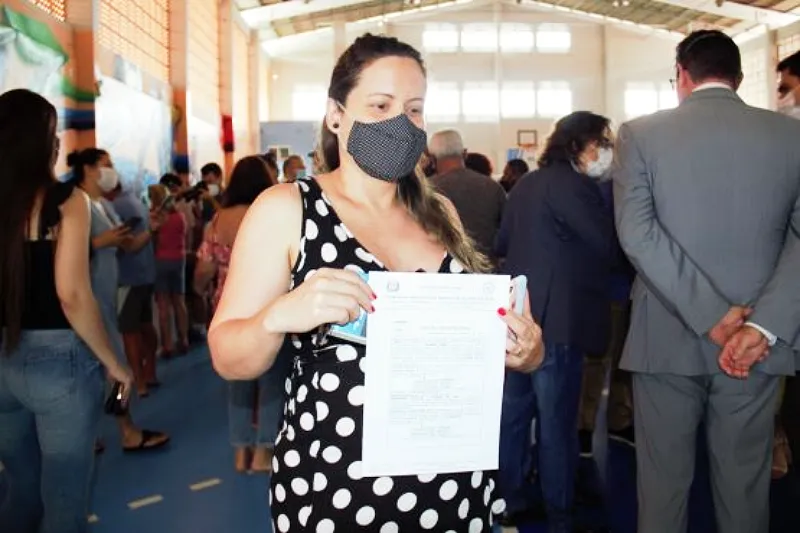 mulher usando máscara posa para foto com documento de escritura pública