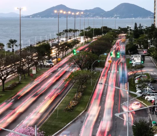 Inflação chega próximo de 4% em 2022 em Florianópolis carros passando na beira-mar deixam rastro de luz; mar ao fundo - Prefeitura de Florianópolis apresenta Plano Diretor em audiência pública