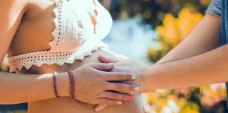 homem coloca as mãos sobre barriga de grávida em ambiente externo com flores