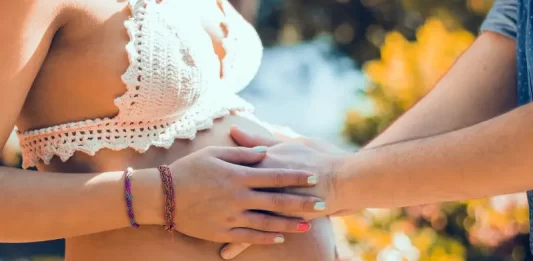 Justiça Federal autoriza médicos a fazerem partos domésticos em SC homem coloca as mãos sobre barriga de grávida em ambiente externo com flores