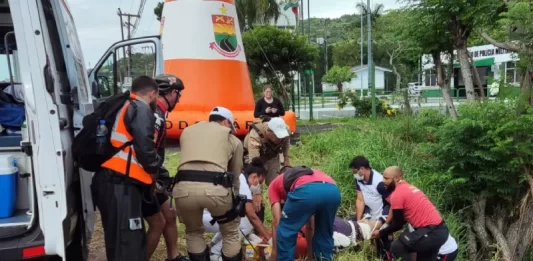 equipes de resgate retirando corpo ao lado de barrando com árvores - Motociclista morre em frente ao posto policial da SC-401