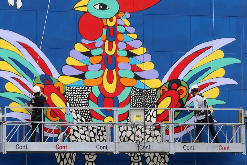 duas pessoas em andaime pintando o gigantesco mural de meyer filho em lateral de prédio no centro de florianópolis