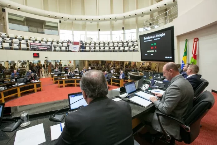 deputados na mesa da presidência da alesc com bancadas e demais parlamentares em baixo ao fundo