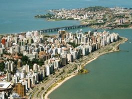foto aérea de florianópolis, com prédios e orla da beira-mar em primero plano, pontes e região do continente