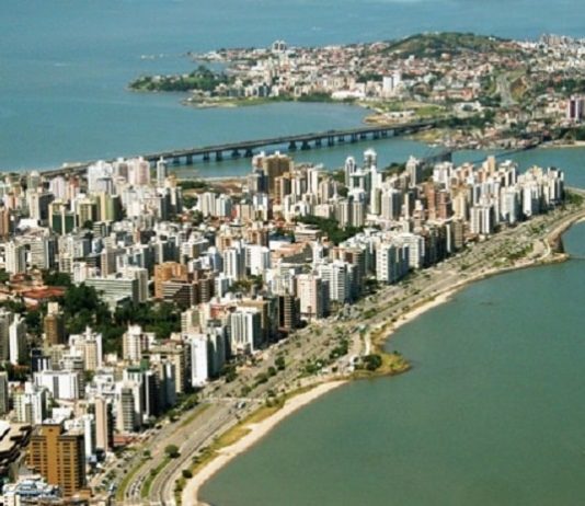 foto aérea de florianópolis, com prédios e orla da beira-mar em primero plano, pontes e região do continente