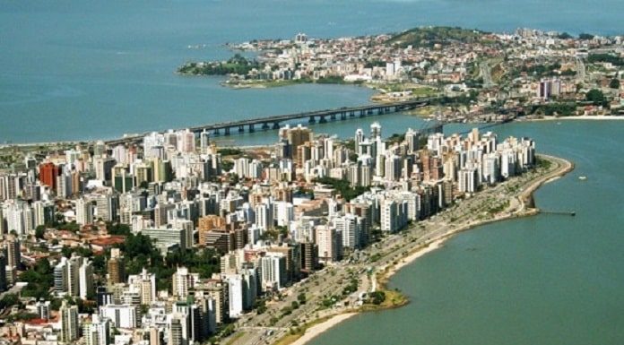 foto aérea de florianópolis, com prédios e orla da beira-mar em primero plano, pontes e região do continente