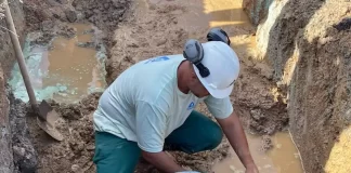 operário da casan em frente ao tubo cortado dentro de buraco com lama e água