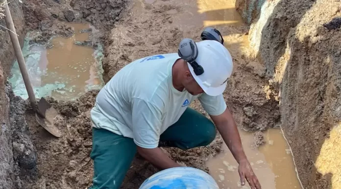 operário da casan em frente ao tubo cortado dentro de buraco com lama e água