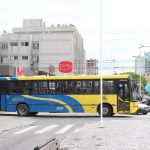 Vista lateral de um ônibus coletivo azul e amarelo cruzando uma avenida com um calçadão no meio