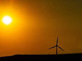 Imagem ilustra calor intenso, com sol forte no horizonte e um aerogerador em silhueta, representando altas temperaturas e clima seco.