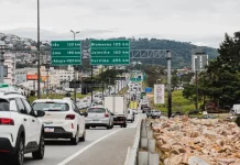 Vista da Via Expressa com tráfego de veículos; ao lado, a via marginal exibe pedras instaladas para impedir ocupações irregulares.