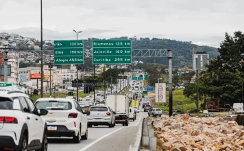 Vista da Via Expressa com tráfego de veículos; ao lado, a via marginal exibe pedras instaladas para impedir ocupações irregulares.