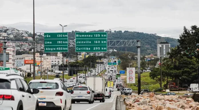 Vista da Via Expressa com tráfego de veículos; ao lado, a via marginal exibe pedras instaladas para impedir ocupações irregulares.