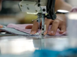 Economia criativa cresce 30% em SC e gera 180 mil empregos formais Uma mão feminina está posicionada sobre uma máquina de costura, guiando cuidadosamente um tecido rosa-claro. Os dedos tocam levemente o pano, enquanto a agulha da máquina faz o movimento de costura. A cena transmite concentração e delicadeza, com destaque para os detalhes do tecido e da máquina em funcionamento.