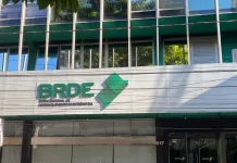 Fachada moderna do prédio do BRDE, com paredes de vidro e logotipo em destaque na entrada