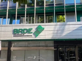 Fachada moderna do prédio do BRDE, com paredes de vidro e logotipo em destaque na entrada