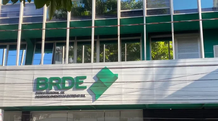 Fachada moderna do prédio do BRDE, com paredes de vidro e logotipo em destaque na entrada