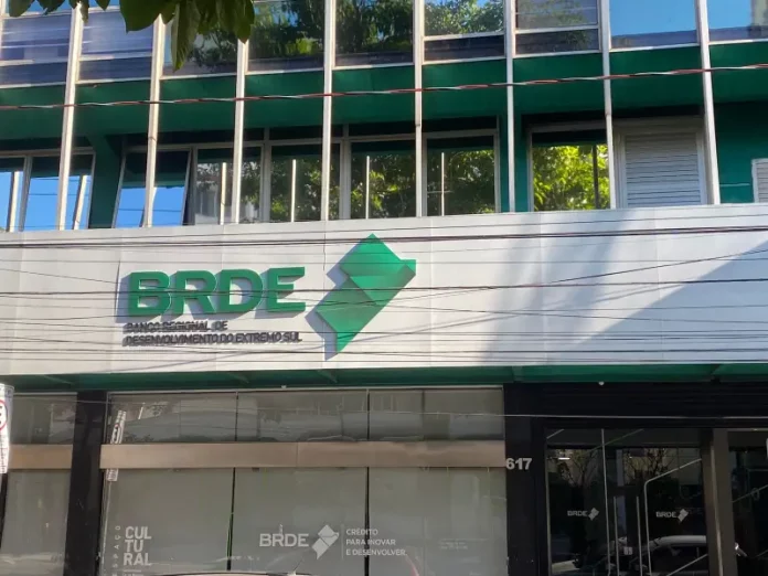 Fachada moderna do prédio do BRDE, com paredes de vidro e logotipo em destaque na entrada