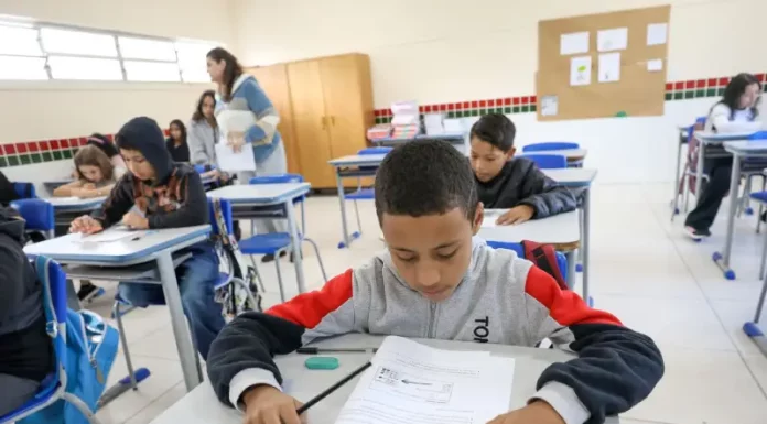 Alunos participam de avaliação em sala de aula no programa Educação Levada a Sério, enquanto a professora circula acompanhando o desempenho.