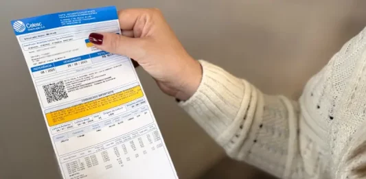 Conta de luz terá alta de 13,53% a partir de 22 de agosto Mãos de uma mulher com blusa branca e unhas pintadas de vermelho seguram uma conta de luz.