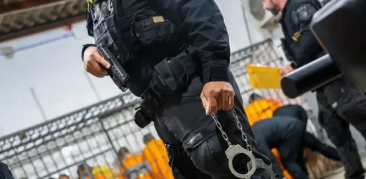 Serviço de escolta da Polícia Penal de SC movimenta mais de 2,5 mil presos sem uma única intercorrência Escolta da Polícia Penal de SC: agente armado com pistola e algemas, com detentos ao fundo em operação de transferência.