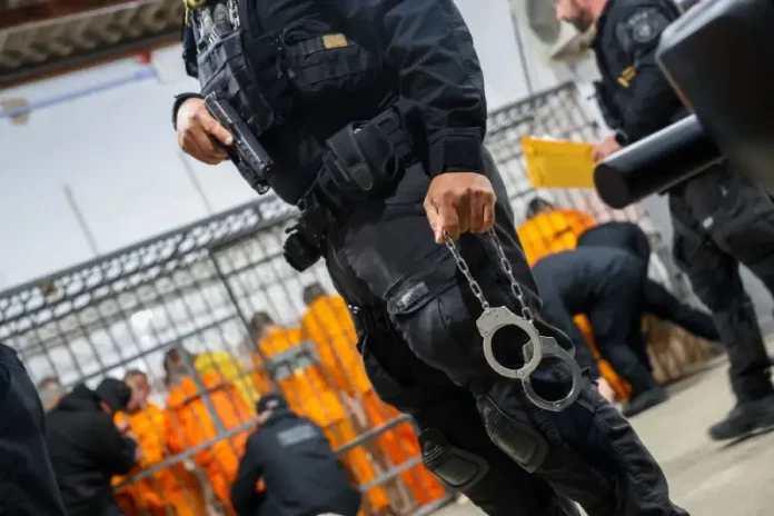 Escolta da Polícia Penal de SC: agente armado com pistola e algemas, com detentos ao fundo em operação de transferência.