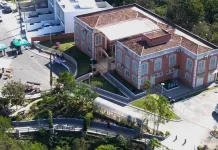 Foto aérea da sede do Jardim Botânico de São José. A construção é de tijolos à vista, com telhado em duas águas. Em frente ao prédio, há árvores de médio porte que compõem a paisagem natural do local.