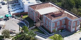 Foto aérea da sede do Jardim Botânico de São José. A construção é de tijolos à vista, com telhado em duas águas. Em frente ao prédio, há árvores de médio porte que compõem a paisagem natural do local.