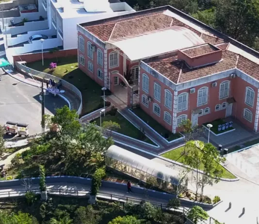 Foto aérea da sede do Jardim Botânico de São José. A construção é de tijolos à vista, com telhado em duas águas. Em frente ao prédio, há árvores de médio porte que compõem a paisagem natural do local.