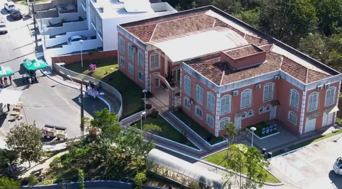 Foto aérea da sede do Jardim Botânico de São José. A construção é de tijolos à vista, com telhado em duas águas. Em frente ao prédio, há árvores de médio porte que compõem a paisagem natural do local.