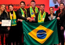 Representantes da Next Shipping posam segurando a bandeira do Brasil e exibindo medalhas e o certificado recebidos durante a cerimônia de premiação do ranking Great Place To Work 2025, em reconhecimento à excelência na gestão de pessoas.