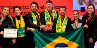 Representantes da Next Shipping posam segurando a bandeira do Brasil e exibindo medalhas e o certificado recebidos durante a cerimônia de premiação do ranking Great Place To Work 2025, em reconhecimento à excelência na gestão de pessoas.