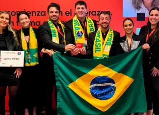 Representantes da Next Shipping posam segurando a bandeira do Brasil e exibindo medalhas e o certificado recebidos durante a cerimônia de premiação do ranking Great Place To Work 2025, em reconhecimento à excelência na gestão de pessoas.